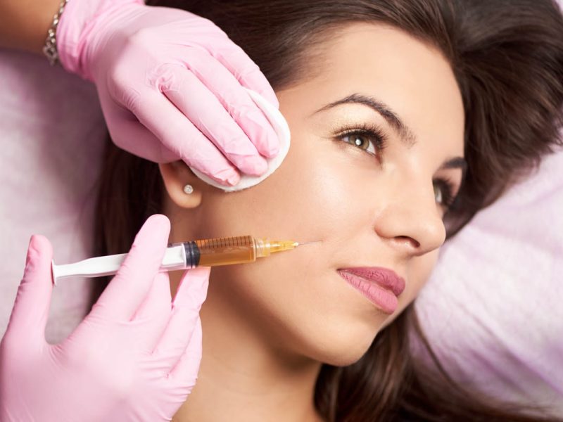 Close-up of beautiful woman getting injection in the cosmetology salon. Doctor in medical gloves with syringe injects cheeks drug.